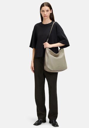 Grau Leder Schultertasche mit weicher Textur, geschwungener Form und kontrastierenden Nähten. Modell trägt ein schwarzes oversized T-Shirt und gestreifte Hosen.