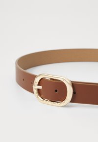 Bruine leren riem met een goudkleurige, ovale gesp, voorzien van een gestructureerde afwerking en meerdere verstelgaten langs de band.