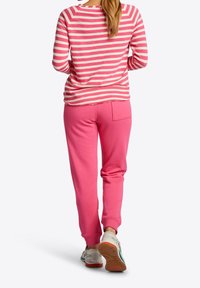 Haut à rayures roses et blanches à manches longues associé à un pantalon de survêtement rose uni avec une poche arrière. Tenue décontractée avec des textures douces.