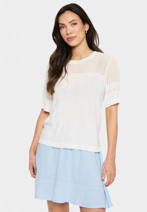 White knit sweater with short sleeves featuring a textured striped pattern at the shoulders. Paired with a light blue skirt.
