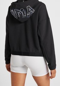 Sweat à capuche court noir avec une capuche ornée d'un texte contour multicolore au dos. Confectionné dans un tissu doux, assorti à un short blanc.