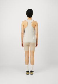 Svijetlosmeđi majica bez rukava s dizajnom racerback, u kombinaciji s bež prilagođenim šortsevima. Materijal izgleda mekano i glatko, pogodno za aktivnu odjeću.
