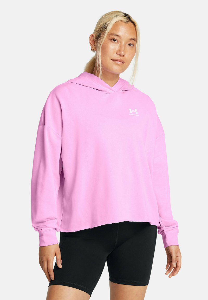Sudadera rosa con corte holgado y mangas largas, con un bolsillo canguro y detalle del logo en blanco en el pecho. Combinada con pantalones cortos negros.