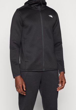 Schwarzer Reißverschluss-Hoodie aus strukturiertem Stoff, mit hohem Kragen, Kapuze und zwei Seitentaschen. Logo auf der linken Brust.