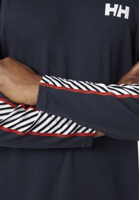 Camisa de manga larga de color azul marino oscuro con tejido texturizado, puños a rayas blancas y negras, y un acento rojo a lo largo de la costura.