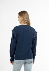Felpa navy con rouches sulle spalle, adornata con bottoni dorati, polsini e orlo a coste. Materiale morbido e vestibilità comoda.