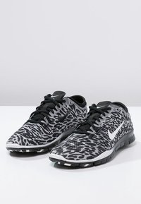 Sort-hvide Nike-sko med et mønstret design, stofoverdel af mesh, matchende snørebånd og gummisål. Har en fremtrædende Swoosh-logo på siden.