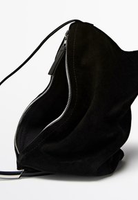 Black suede bag featuring a zip closure, soft texture, and a single shoulder strap. Curved shape with visible stitching detail.