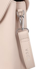 Světlobéžová kožená taška s kovovou sponou v odstínu stříbra a texturovaným popruhem s raženým označením "VUCH". Hladký povrch, minimalistický design.