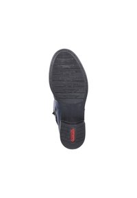 Semelle en caoutchouc noir avec texture antidérapante, présentant un accent rouge. Le design comprend de légers contours et rainures pour une meilleure adhérence.