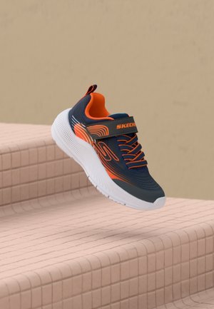 Granatowo-pomarańczowy sneaker Skechers z białą podeszwą, sznurowadłami i paskiem unoszący się nad beżowymi, kafelkowymi schodami.