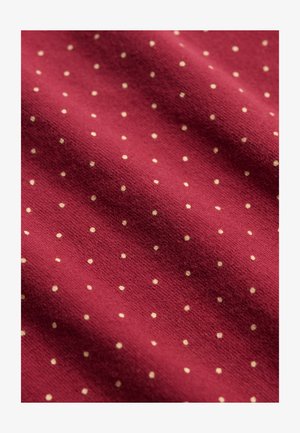 Tissu rouge avec de petits pois blancs régulièrement espacés, montré en gros plan, mettant en valeur la texture et le motif.