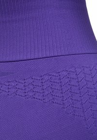 Paarse sportleggings met een geribbelde textuur en een zigzagpatroon op het onderste deel, gemaakt van flexibel, ademend materiaal.