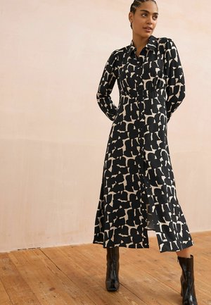 Czarna i beżowa sukienka w wzory z długimi rękawami, z zapięciem na guziki i sylwetką w kształcie litery A, zestawiona z czarnymi botkami za kostkę.