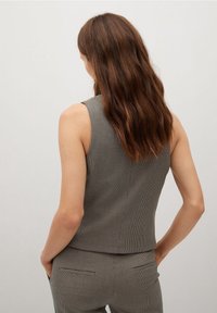 Top sin mangas a cuadros grises con un diseño ceñido. Presenta una textura sutil y una costura en la parte trasera. Bolsillos visibles en la cintura.