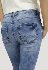 Blå denimjeans med en figurnära design, två bakfickor och en något blekt textur. Midjan har standardhöjd.