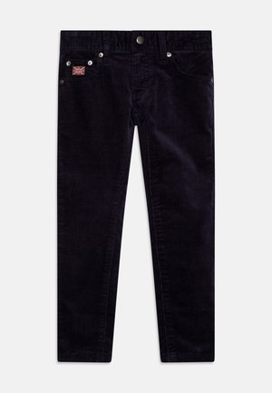 Pantalon en velours côtelé bleu marine avec poches avant, fermeture par bouton métallique et un petit patch drapeau Union Jack sur la poche droite.
