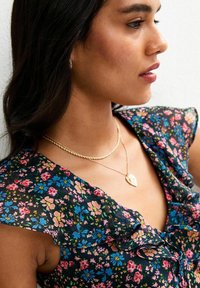 Vestido con estampado floral, mangas con volantes, fondo azul marino y flores de colores múltiples. Presenta cadenas de oro en capas y un colgante en forma de corazón.