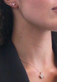 Orecchini a forma di cuore in oro rosa e collana abbinata con pendente in pietra trasparente. Finitura metallica liscia, design della catena delicato.