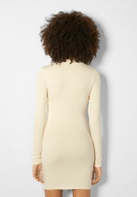 Polven mittainen, pitkähihainen mekko, joka on valmistettu kevyestä, pehmeästä beigestä kankaasta. Siipimallinen muotoilu ja pyöreä kaula-aukko. Sileä pinta ilman näkyviä kuvioita.