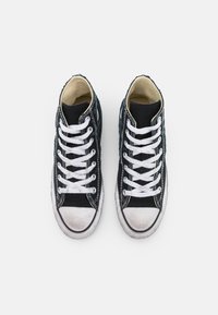 Zapatillas altas hechas de lona negra con punta de goma blanca, cordones blancos y lateral texturizado. Presentan un suave forro interior.