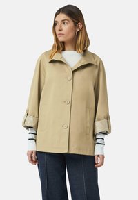 Beżowa kurtka przeciwdeszczowa z kołnierzem, guzikowym zapięciem z przodu, dwoma bocznymi kieszeniami i wzorzystymi mankietami; charakteryzuje się luźnym krojem i gładką fakturą.