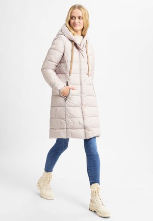 Gepolsterte, hellbeige Parka mit Kapuze, ausgestattet mit einem Reißverschluss auf der Vorderseite und Taschen, kombiniert mit blauen Jeans und beige Schnürstiefeln.