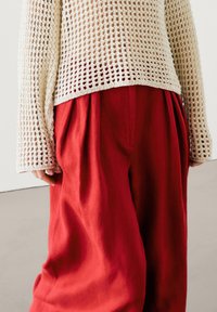 Pull crème en maille ajourée à manches longues assorti d'un pantalon large en lin rouge avec plis et texture lisse.
