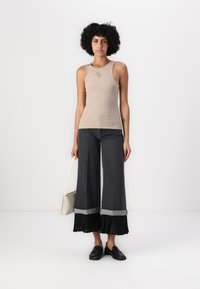 Beige geribbelde tanktop met een logo, gecombineerd met wijde donkere denim broek met plooien in het zwart aan de zoom, en zwarte instap schoenen.