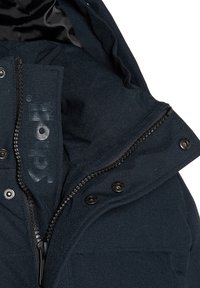 Chaqueta azul marino con cierre frontal de cremallera, botones de presión, tejido texturizado y etiqueta con logo en el interior del cuello.