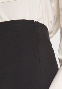 Zwarte kokerrok met een soepele textuur, voorzien van een verborgen rits en minimale stikseldetails, gecombineerd met een lichtgekleurde blouse.