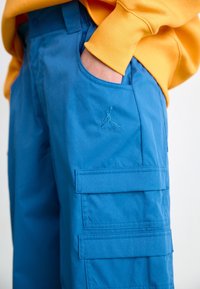 Blå cargobyxor gjorda av lättviktsmaterial, med två sidofickor och en broderad Jumpman-logga på framsidan.