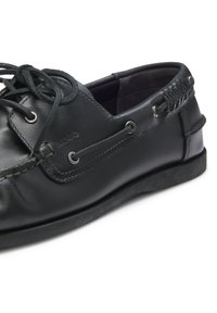 Μαύρο δερμάτινο παπούτσι τύπου boat με κορδόνια μπροστά, μεταλλικές θηλιές στα πλευρά, ραφές και χαμηλή σόλα από καουτσούκ.