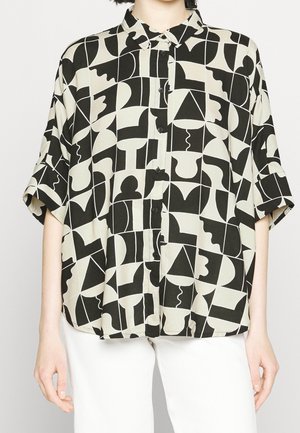 Koszula na krótkim rękawie zapinana na guziki, z czarno-białym abstrakcyjnym geometrycznym wzorem, noszona z białymi spodniami.