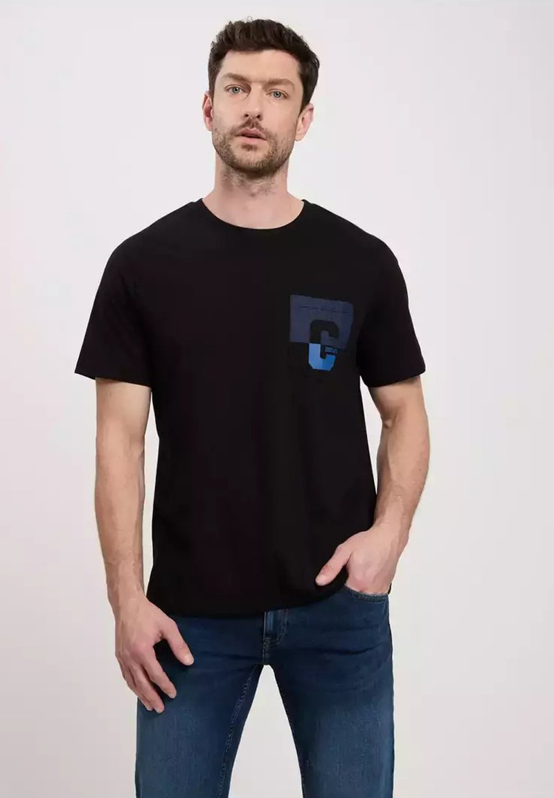 Czarny bawełniany t-shirt z okrągłym dekoltem, z niebieską kieszonką z logo "C". Zestawiony z niebieskimi dżinsami.