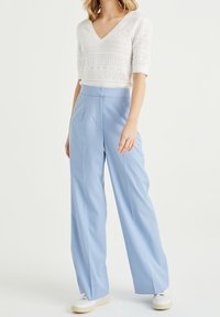 Top de punto blanco de manga corta con escote en V, combinado con pantalones de pierna ancha de color azul claro y zapatillas blancas, con un acabado liso.
