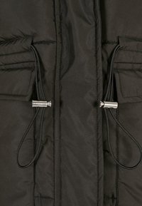 Black puffer jacket fabric with visible stitching, two front pockets, and drawstrings terminating in metallic toggles.