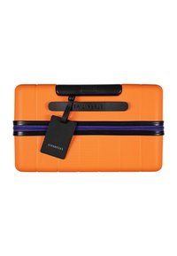 Oranje harde koffer met textuurafwerking, zwarte rits en accenten, voorzien van een bagagetag en merknamen die op de zijkant zijn gedrukt.