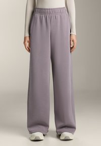 Kalhoty s širokými nohavicemi a elastickým pasem z jemné, tlumené levandulové látky; hladký povrch s bočními kapsami; doplněné lehkými, polstrovanými teniskami.