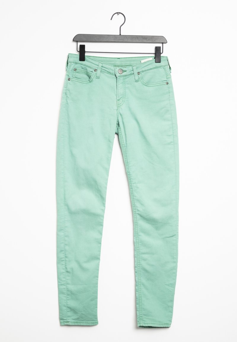 Jean slim vert menthe avec fermeture à bouton et zipper, poches avant et arrière, suspendu à un cintre noir contre un fond blanc.