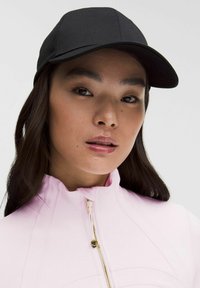 Czarna czapka bejsbolowa z materiału, z zakrzywionym daszkiem. Model nosi różową kurtkę na zamek błyskawiczny z złotym detalem zamka.