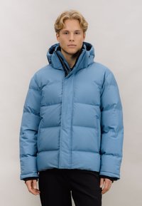 Lyseblå pufferjakke med høy krage, glidelås foran og quiltet design. Har hette og elastiske mansjetter. Stoffet ser glatt og skinnende ut.