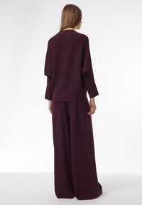 Haut rouge vin ample avec épaules tombantes et pantalon à jambes larges. Tissu lisse avec des coutures minimales, créant une silhouette décontractée.