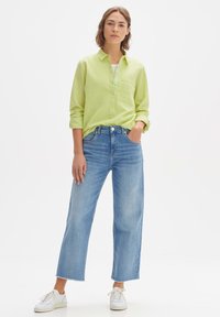 Light green long-sleeve button-up shirt, blue wide-leg jeans, and white sneakers. Shirt has a pocket and rolled-up sleeves. Casual outfit.