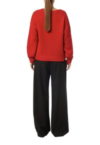 Roter gestrickter Pullover mit weiten Ärmeln und geripptem Saum, kombiniert mit lockeren schwarzen Hosen aus glattem Stoff im weiten Schnitt.