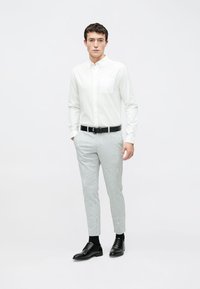 Hvit skjorte med knapper og brystlomme, kombinert med lysegrå, teksturerte, smale bukser og svarte sko med snøring.