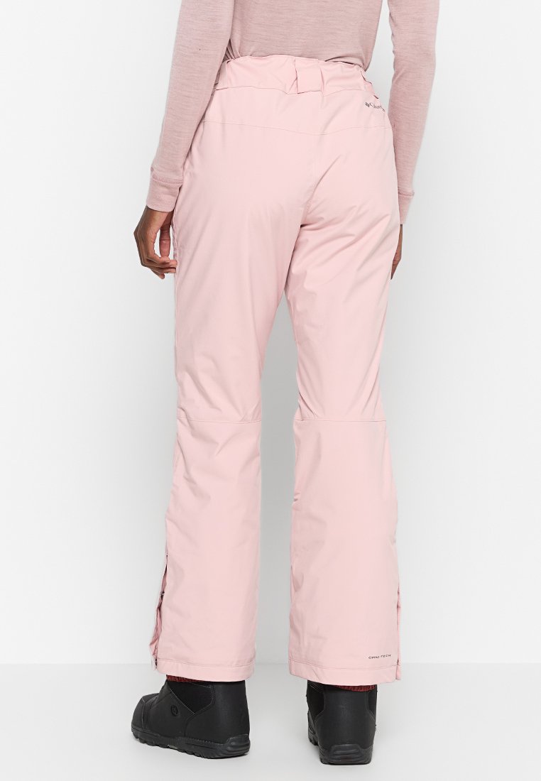 Jasnoróżowe spodnie narciarskie wykonane z materiału wodoodpornego, z prostym krojem nogawki i bocznymi zamkami wentylacyjnymi, w zestawie z czarnym obuwiem.