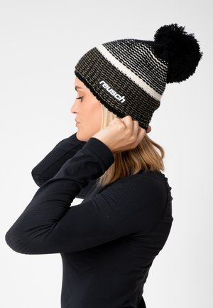 Black and white knit beanie with a pom-pom on top; features a zigzag pattern and a logo label. Material is textured wool blend.
