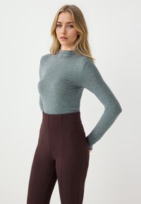 Długo rękawowy, dopasowany top w heathered teal, połączony z wysokim stanem, ciemno brązowymi legginsami z bocznymi szwami i gładką teksturą.