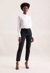 Wit overhemd met lange mouwen, knoopsluiting en brede manchetten, gecombineerd met zwarte jeans met hoge taille en zwarte sandalen met bandjes.